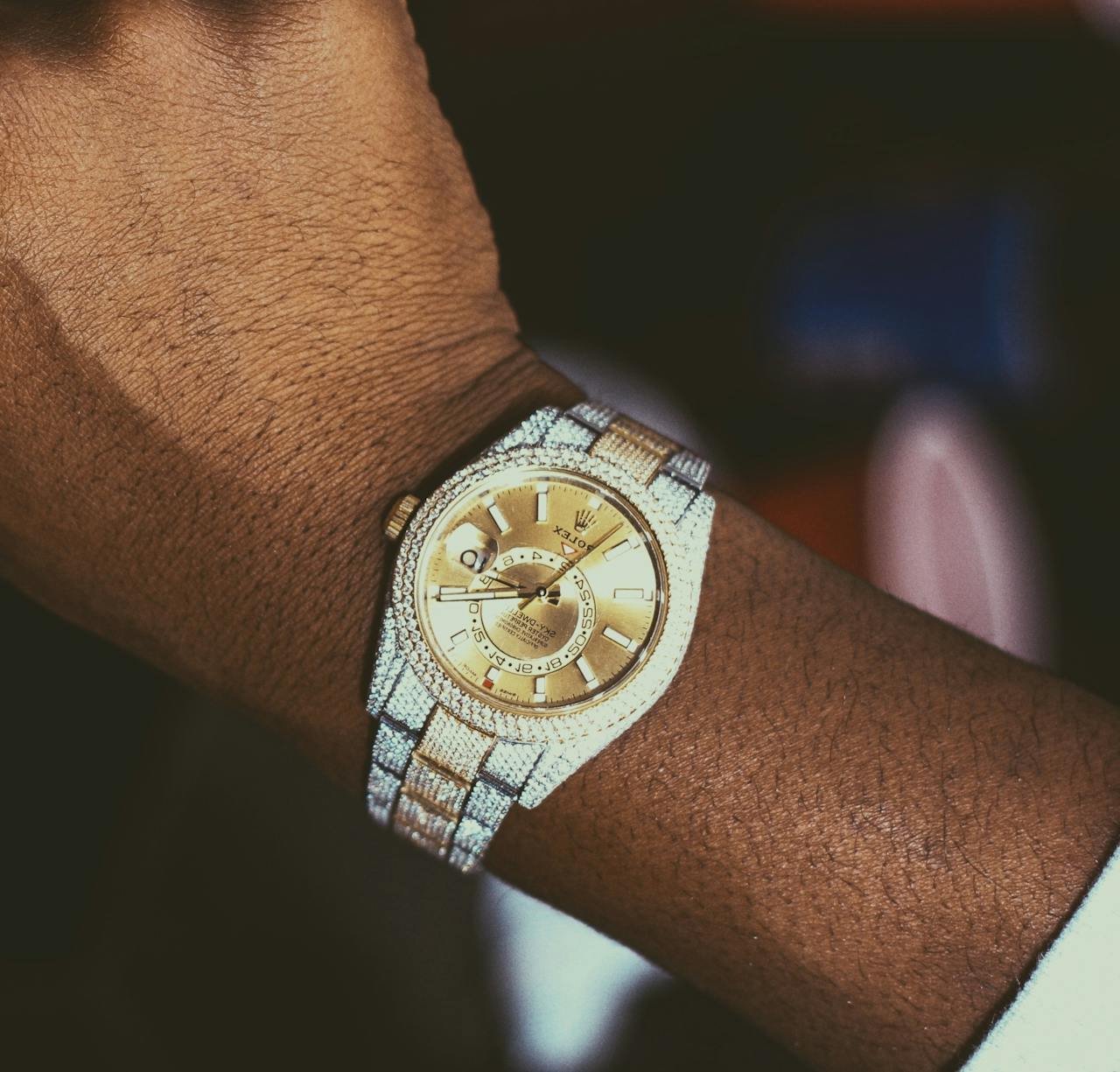 Home - Offiicial Close-up of a luxury gold watch with a diamond-studded bezel on a person's wrist.
