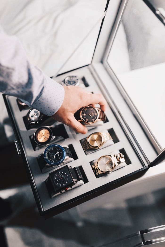 Home - Offiicial A sophisticated display of luxury watches in an elegant case with a hand selecting one.